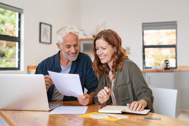 Mature smiling couple sitting and managing expenses at home. Happy senior man and mid woman paying bills and managing budget. Middle aged couple checking accountancy and bills while looking at receipt.