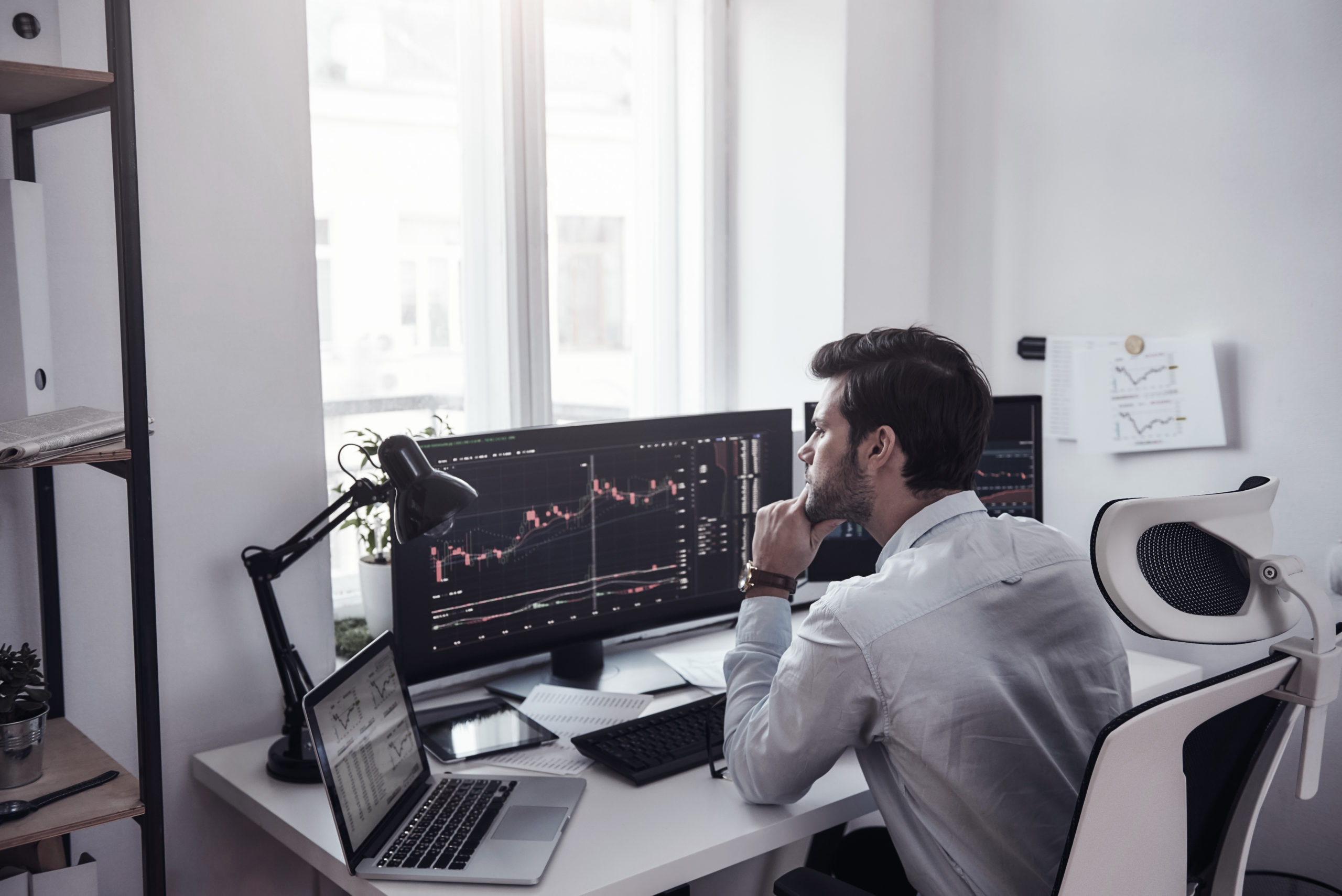 Trading on world markets. Young stock market broker analyzing data and graphs on multiple computer screens while sitting in modern office. Stock exchange. Trade concept. Investment concept